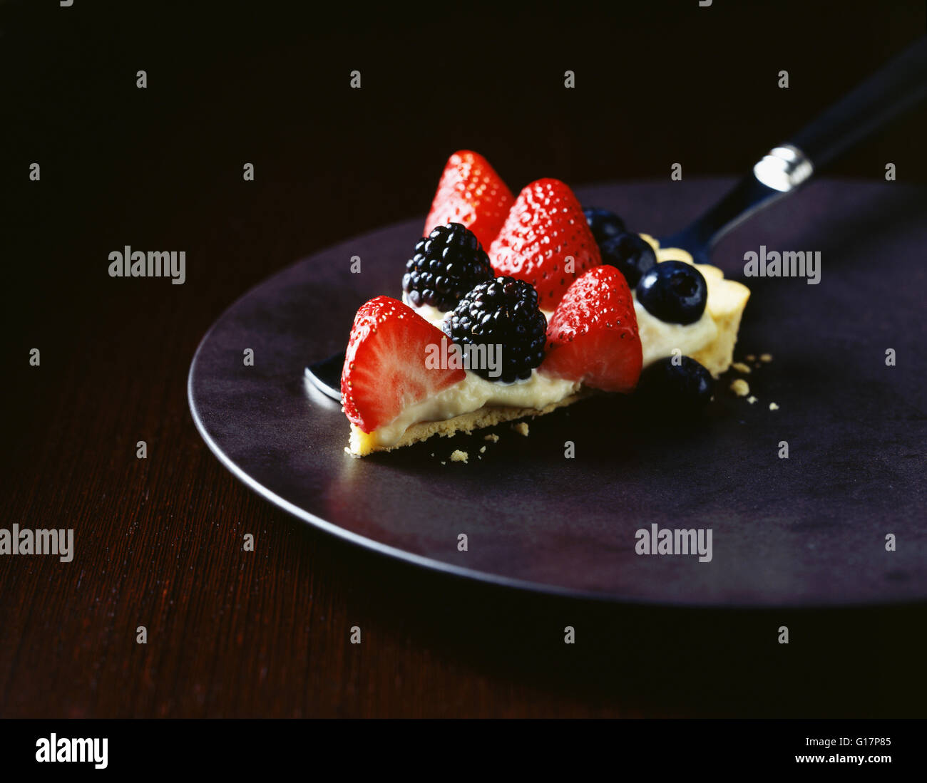 Slice of strawberry, raspberry and blueberry tart on plate Stock Photo