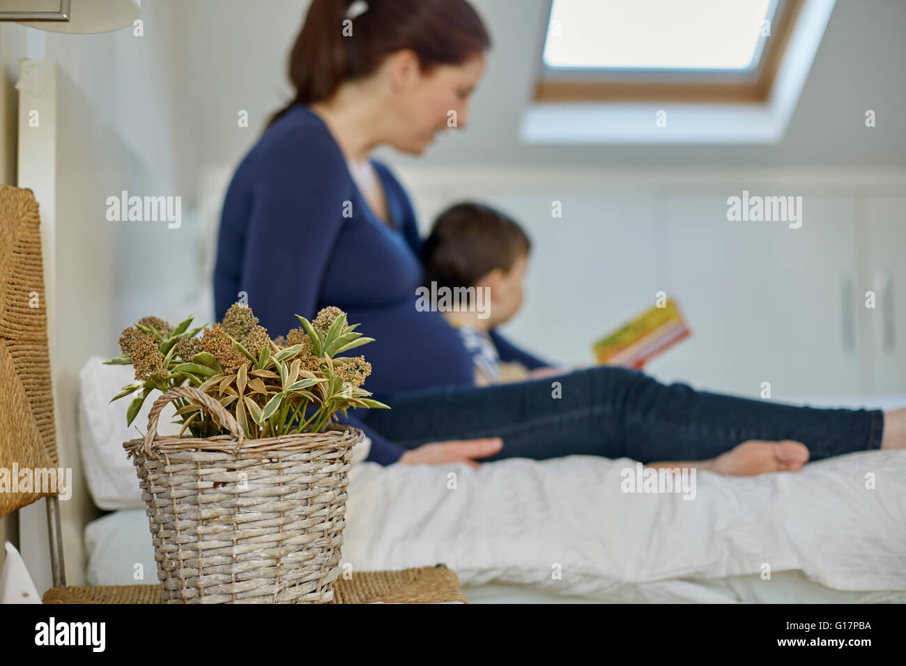 Side view of pregnant mother and baby boy sitting on bed reading book together Stock Photo