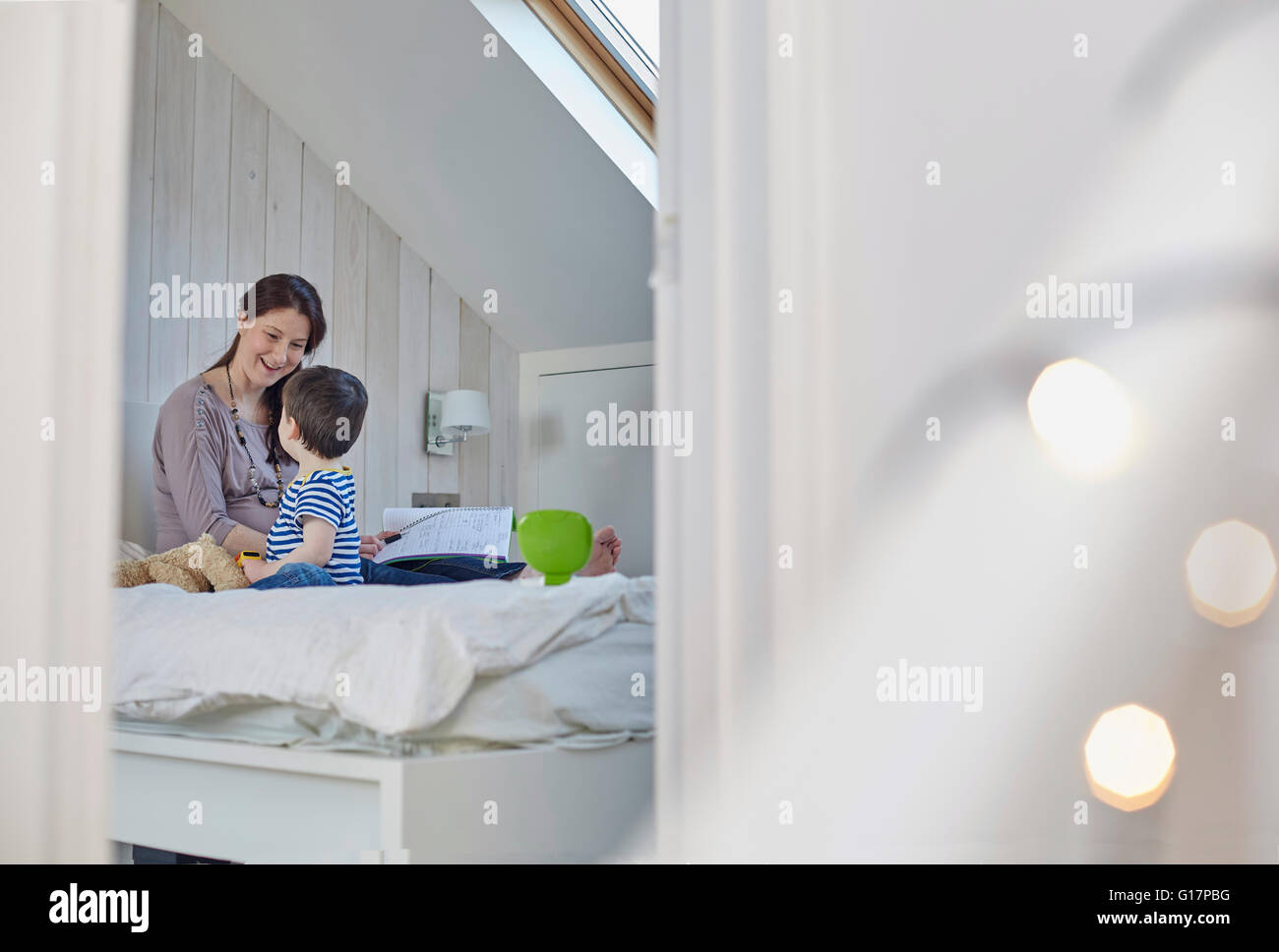 Pregnant mother sitting on bed with baby boy holding book face to face smiling Stock Photo