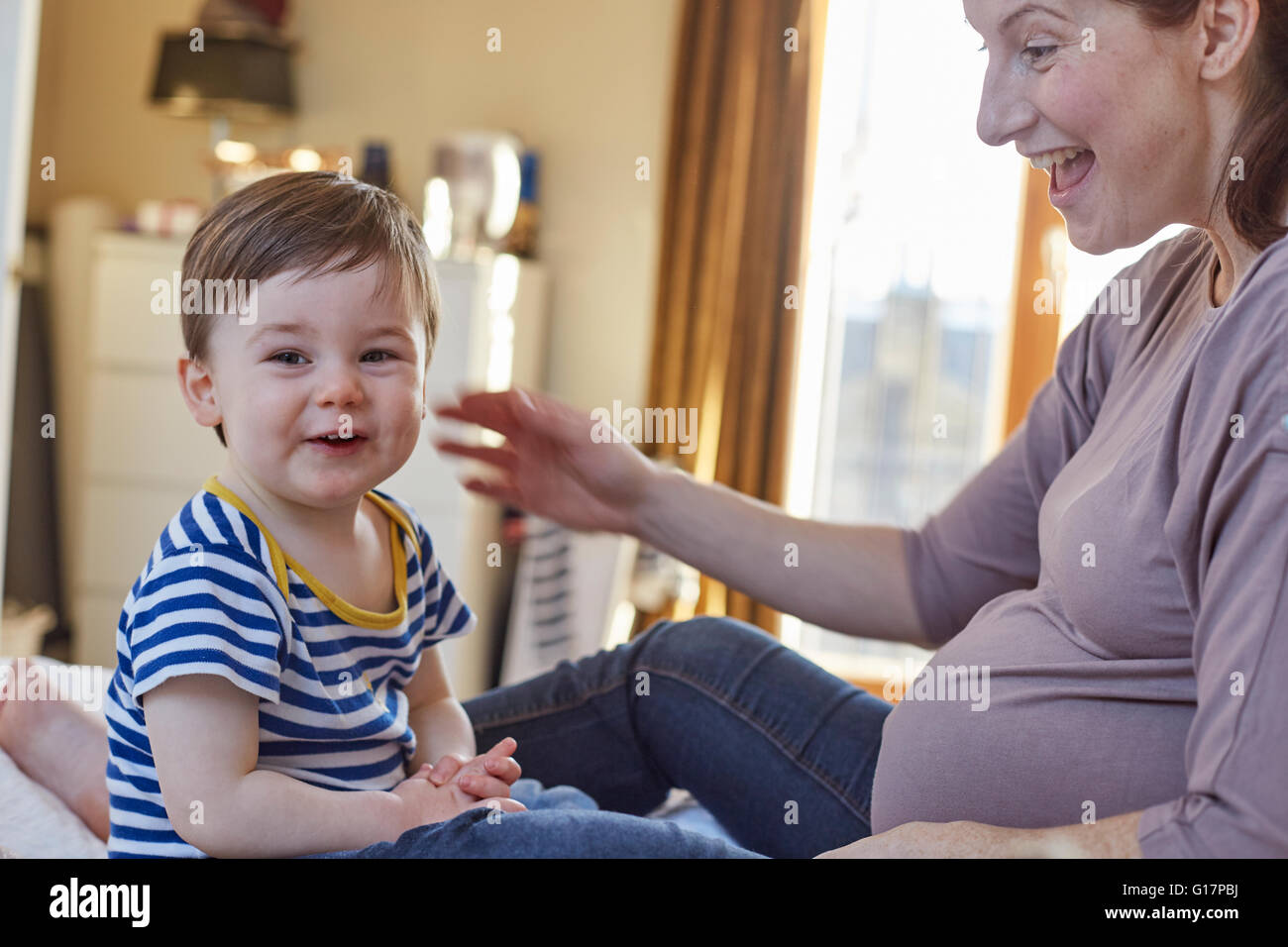 Side view of pregnant mother and baby boy looking at camera smiling Stock Photo