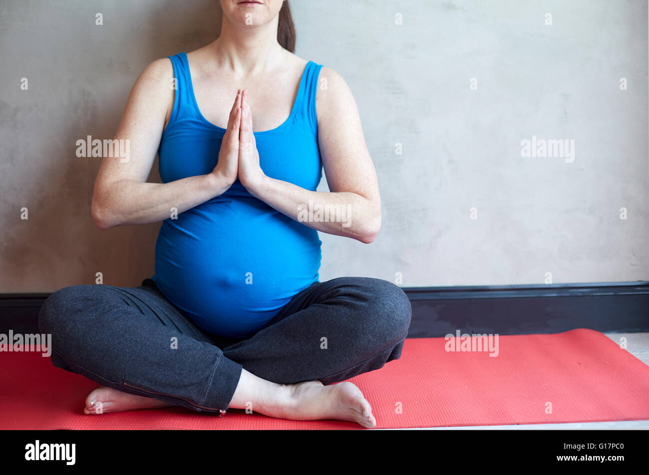 Pregnant woman sitting cross legged, hands together in yoga pose Stock Photo