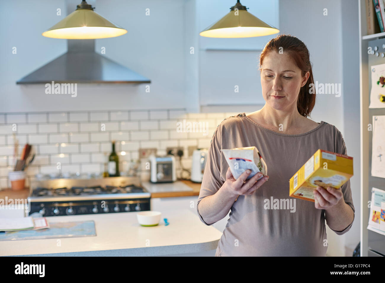 Pregnant woman in kitchen comparing food packets Stock Photo