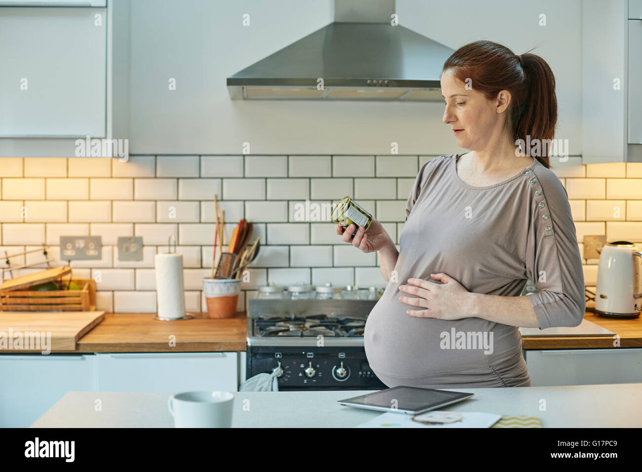 Side view of pregnant woman in kitchen looking at food packaging Stock Photo