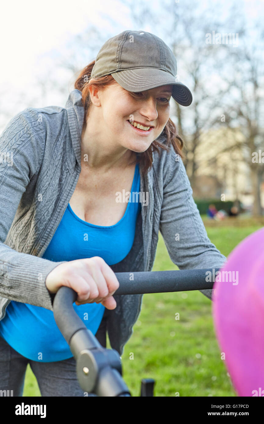 Pregnant woman wearing baseball cap looking at baby in buggy Stock Photo
