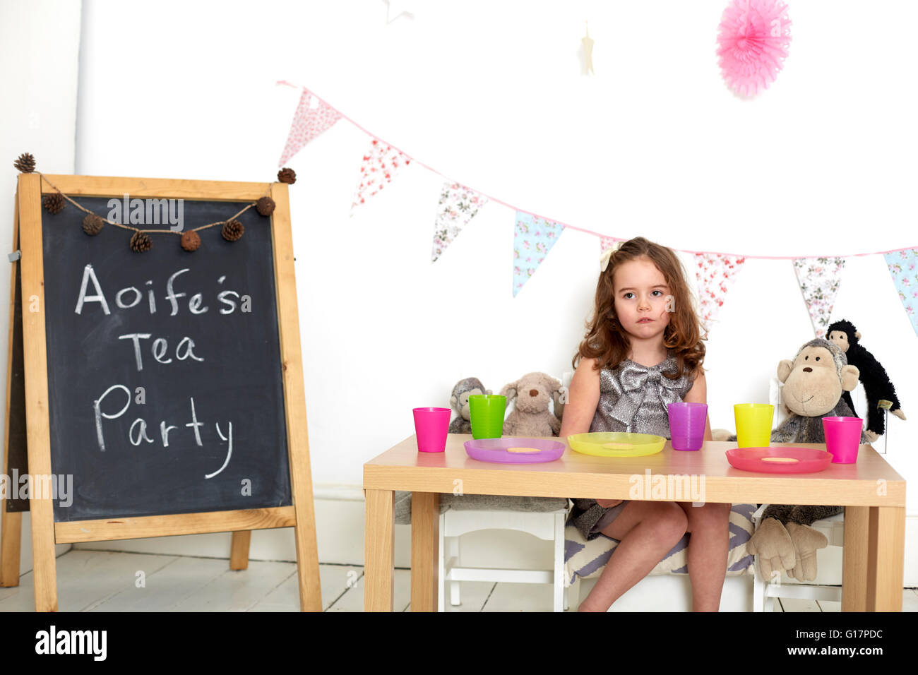 Sad girl at tea party with soft toys Stock Photo