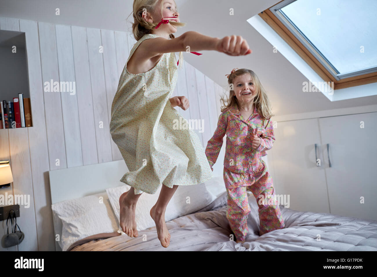 Girls jumping on bed in loft room Stock Photo