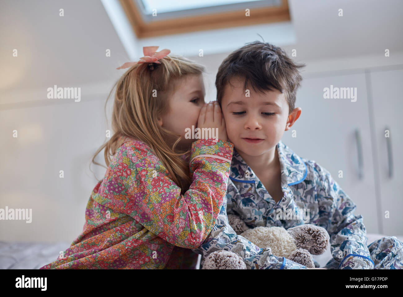 Girl whispering into boy's ear in loft room Stock Photo