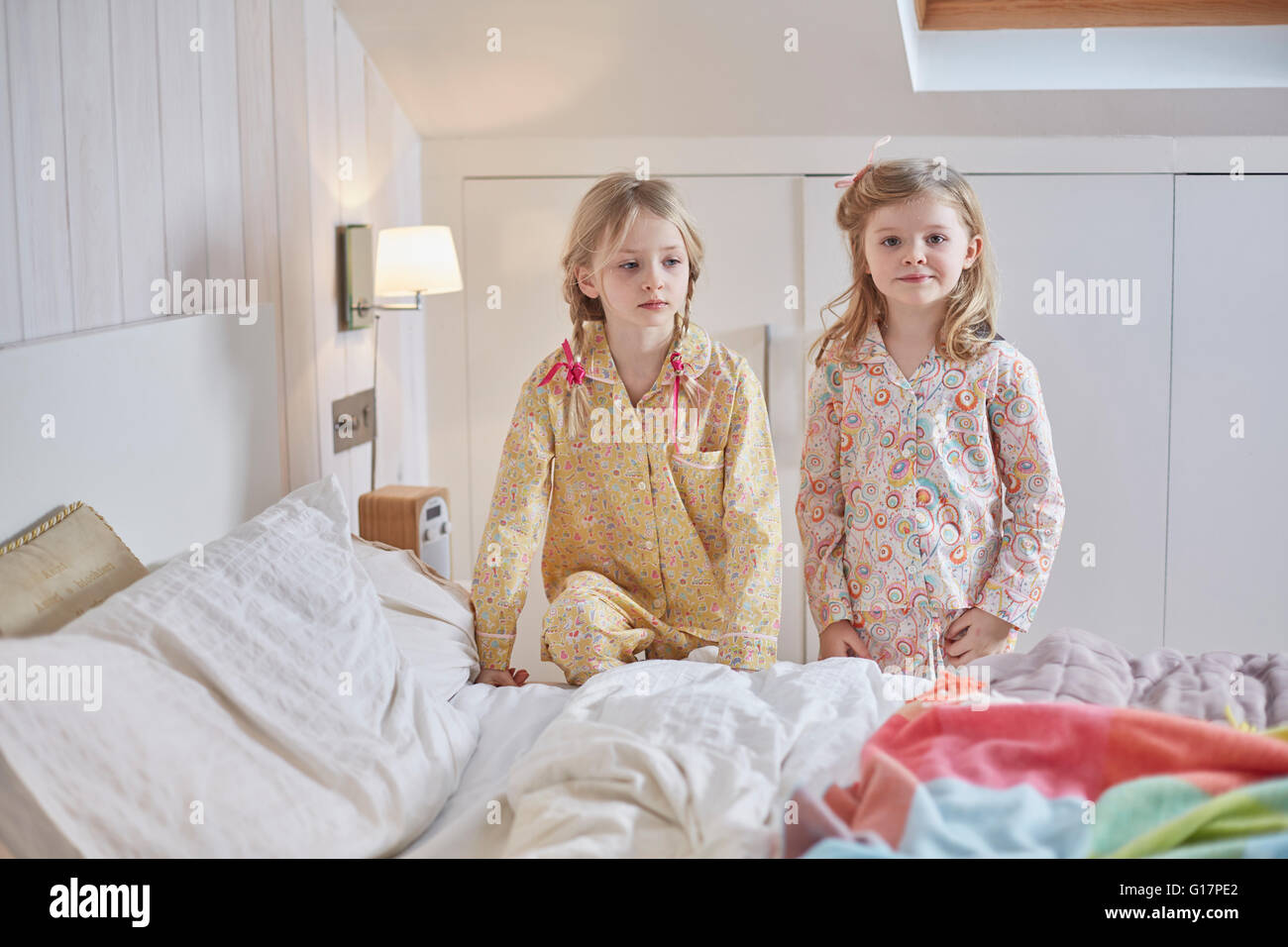 Girls in pyjamas beside bed in loft room Stock Photo