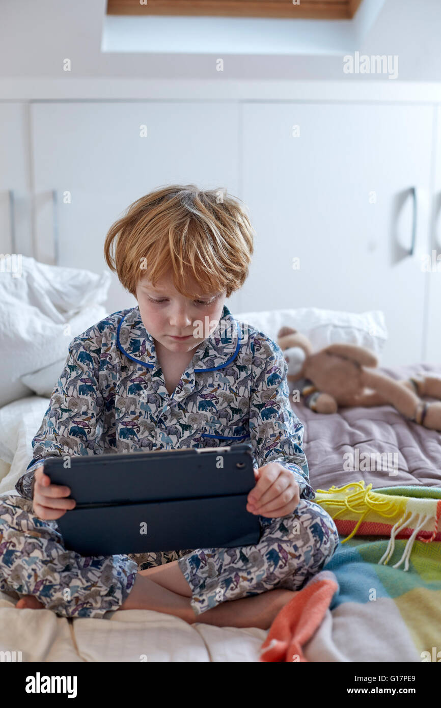 Boy in pyjamas using digital tablet in bed Stock Photo