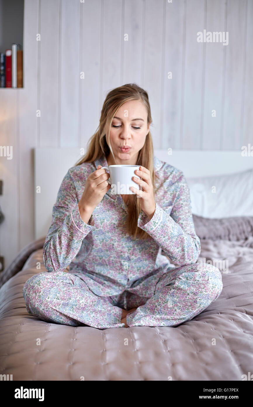 Woman in pyjamas having coffee in bed Stock Photo