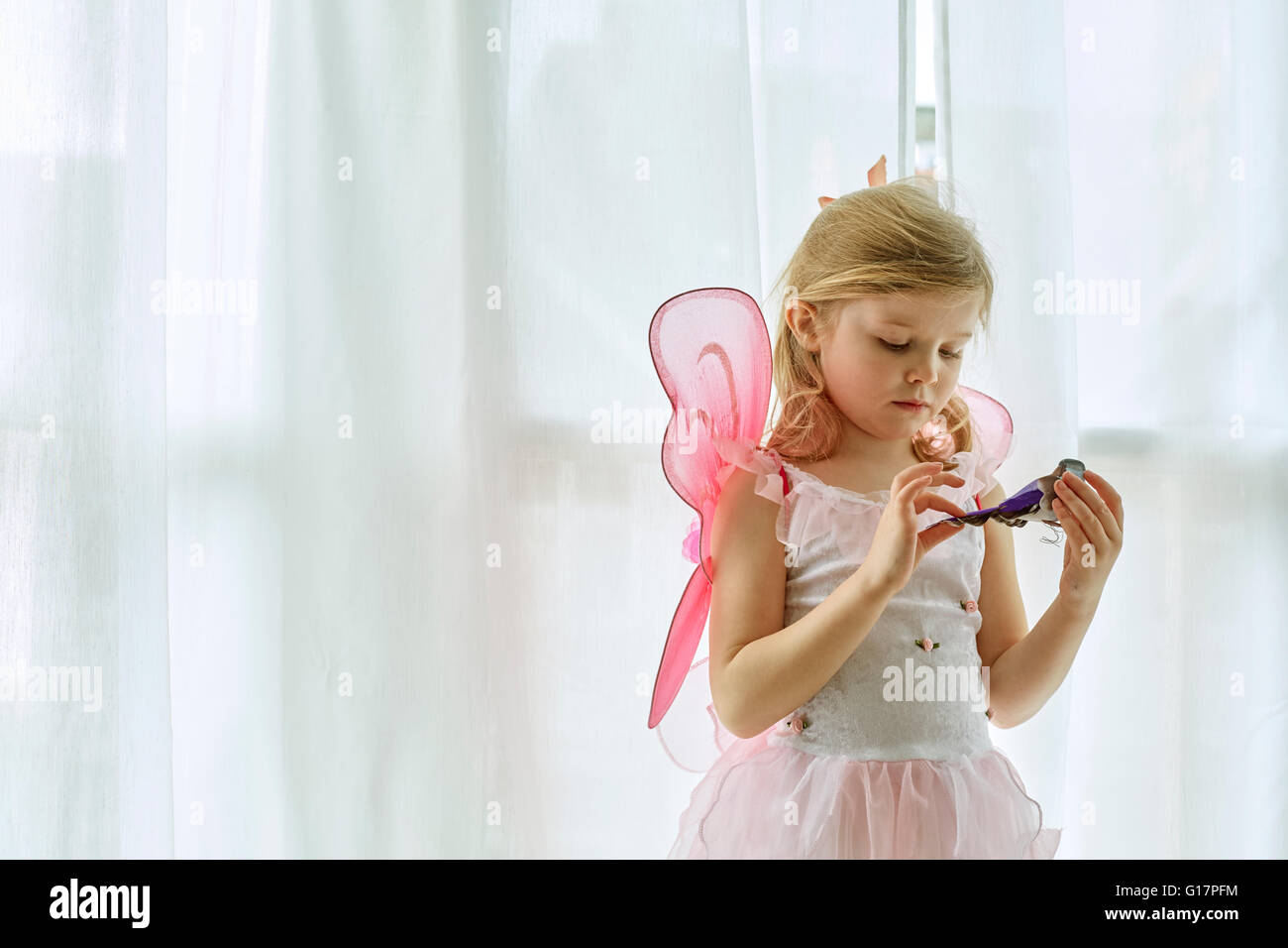 Girl in fairy costume playing by curtain Stock Photo
