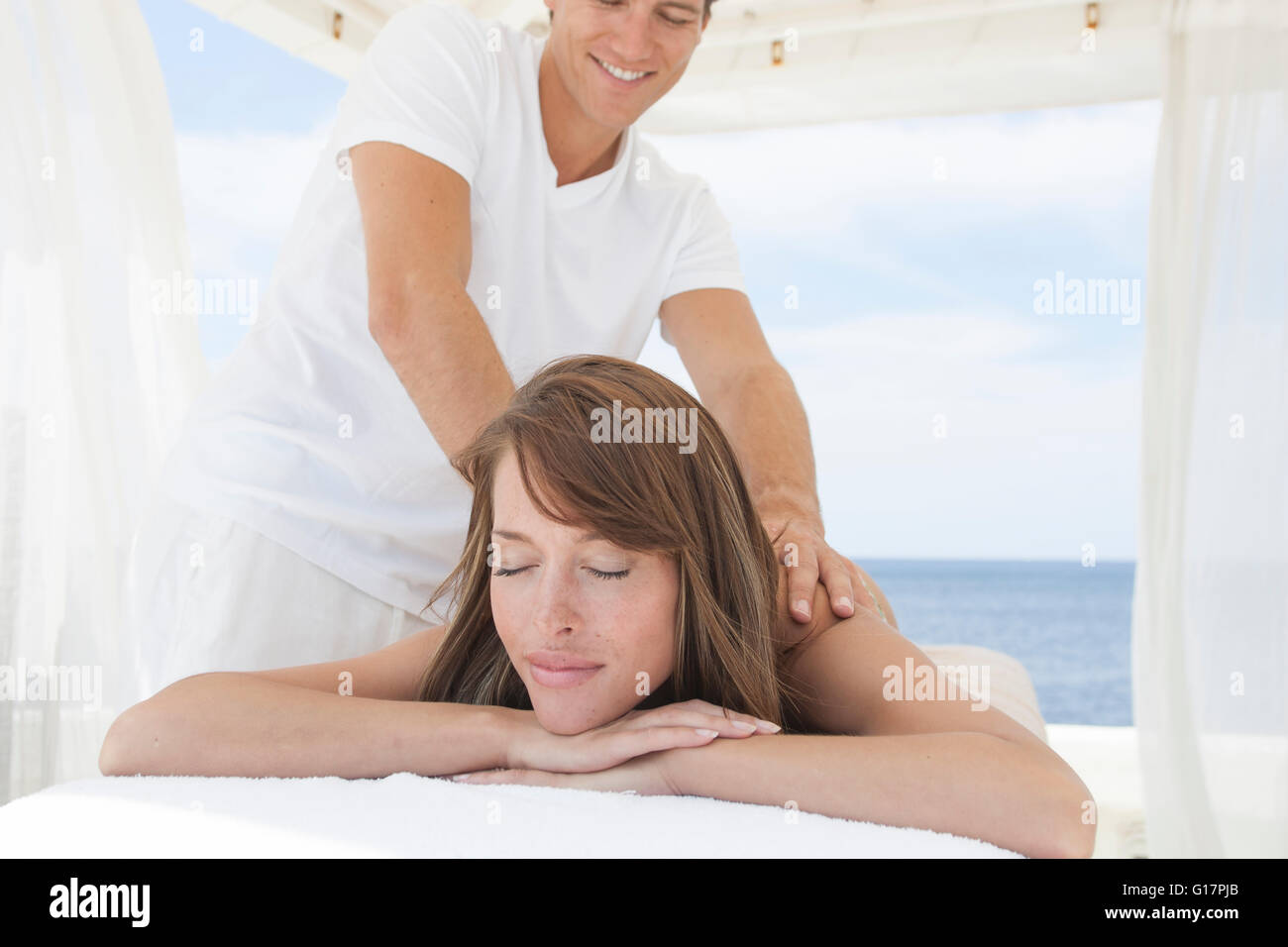 Masseur giving young woman a shoulder massage at beach resort, Majorca
