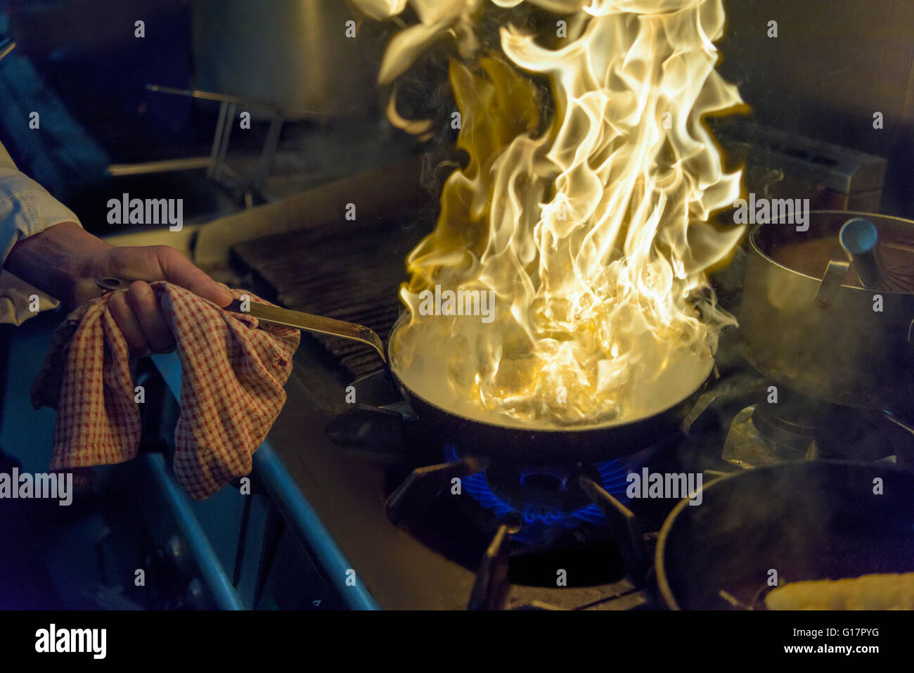 Chef with pan of flames in traditional Italian restaurant kitchen, close up Stock Photo