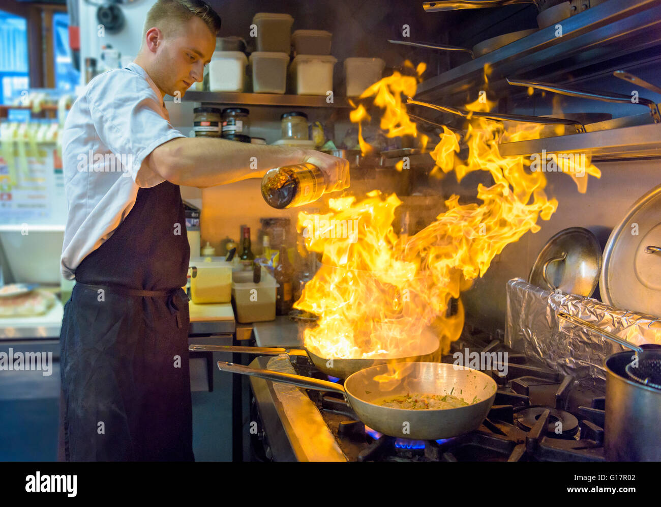 Chef pouring brandy into flaming pan in traditional Italian restaurant kitchen Stock Photo