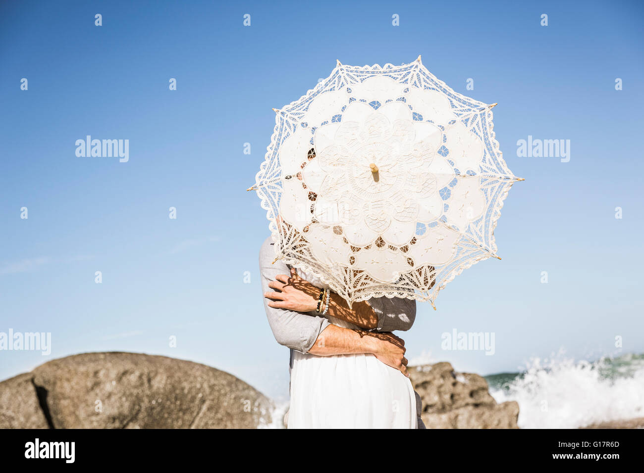 Couple on beach hugging obscured by lace umbrella Stock Photo
