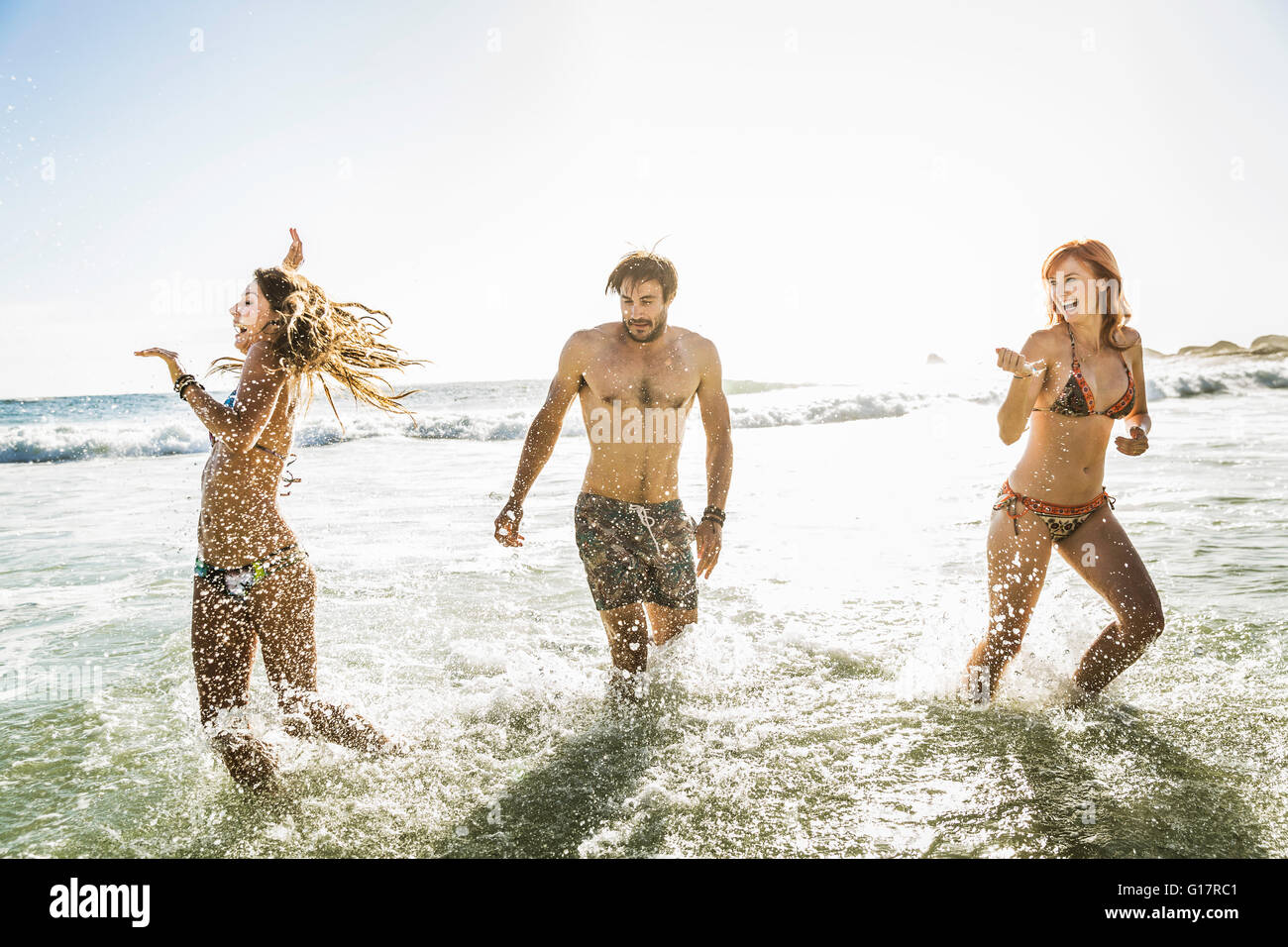 Three adult friends wearing bikinis and swimming shorts splashing in