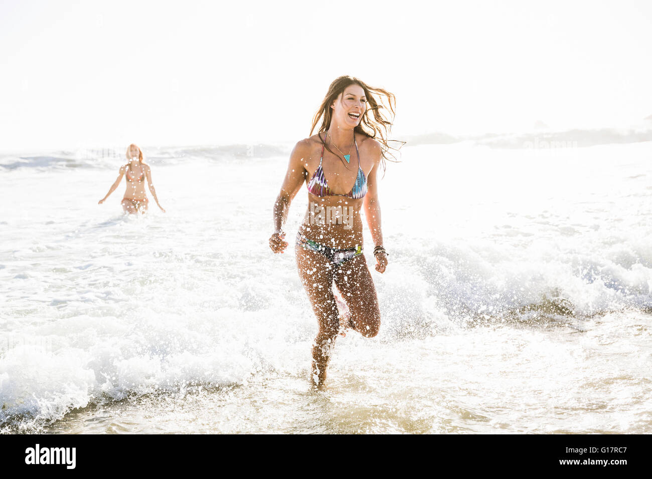 Two women wearing bikini's running in sea, Cape Town, South Africa Stock Photo