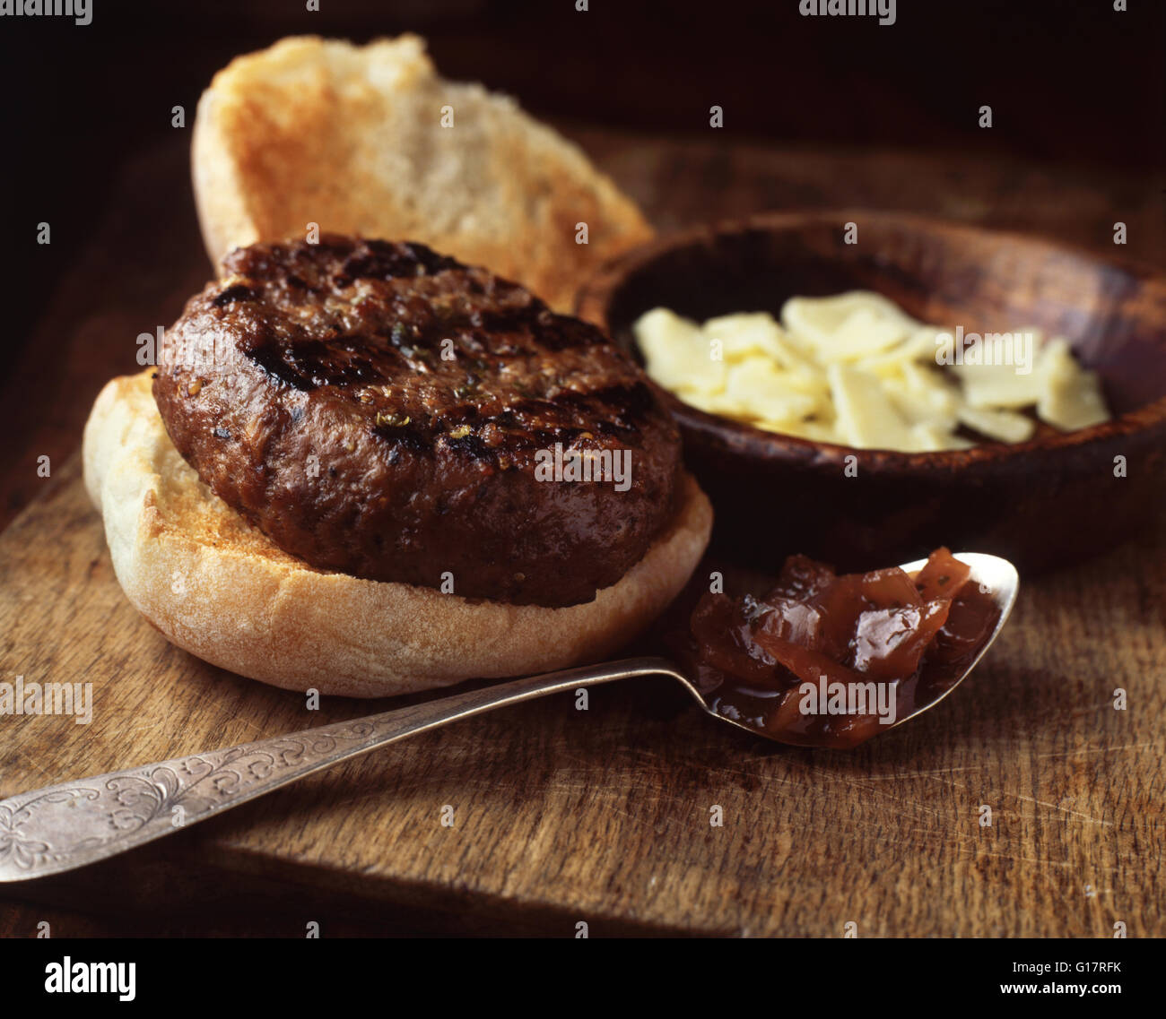 Burger in crusty bun with cheddar cheese and onion relish on wooden cutting board Stock Photo