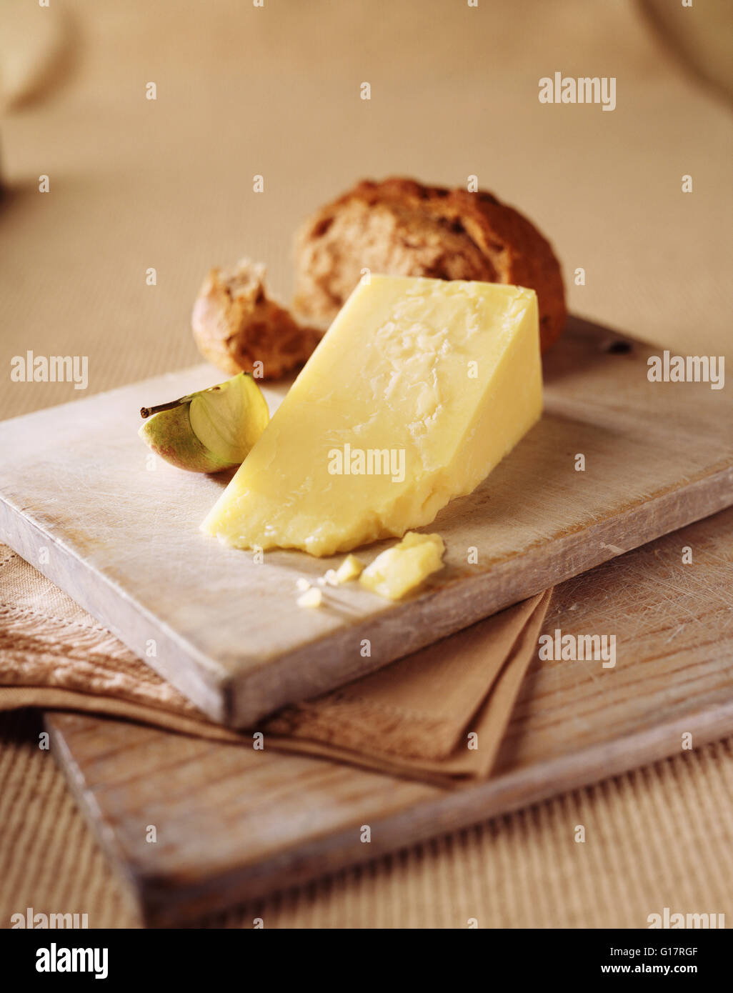 Wedge of mature cheese with apple slice and crusty wholemeal roll on wooden cutting board Stock Photo