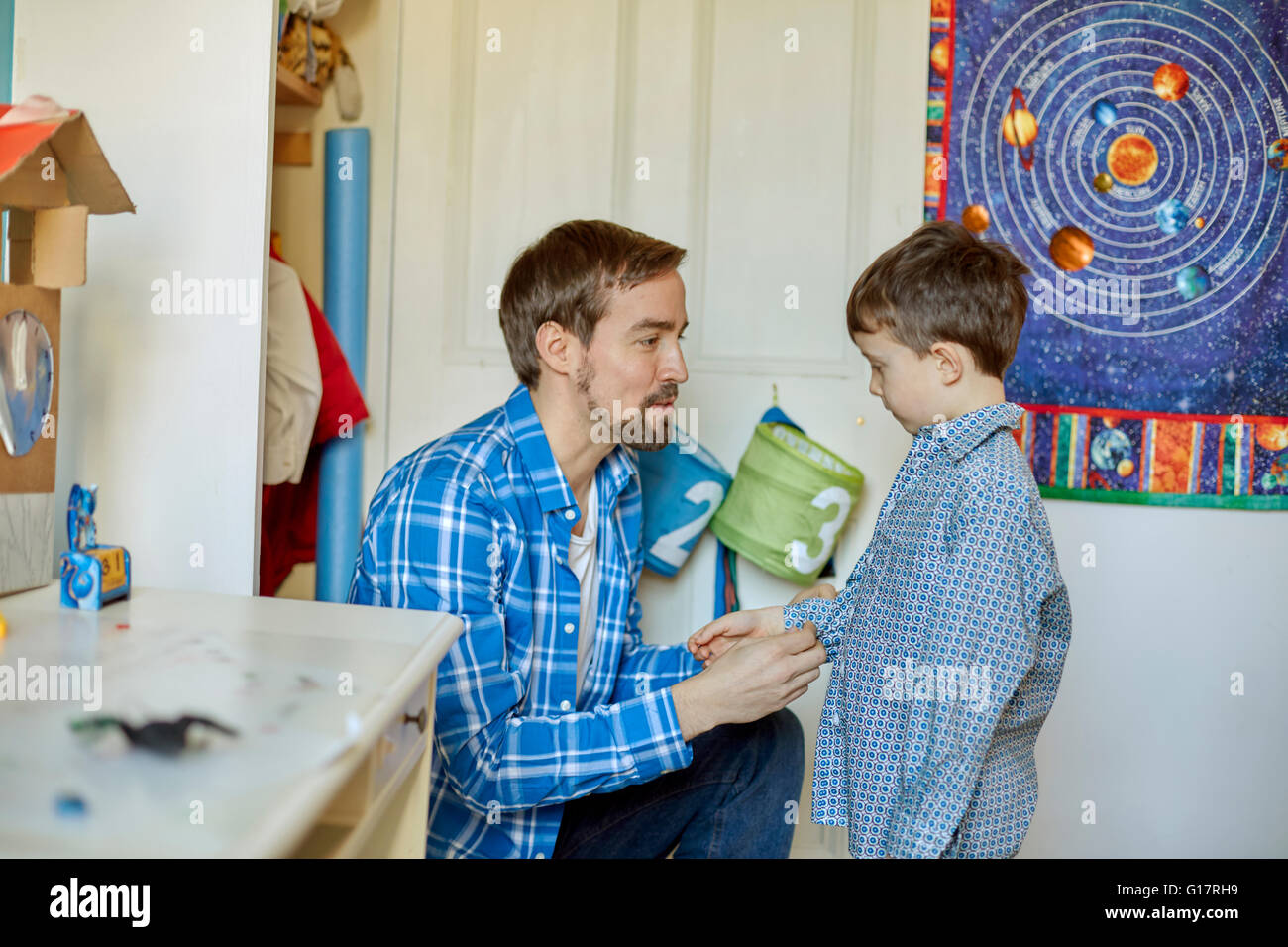 Father helping son button shirt in bedroom Stock Photo