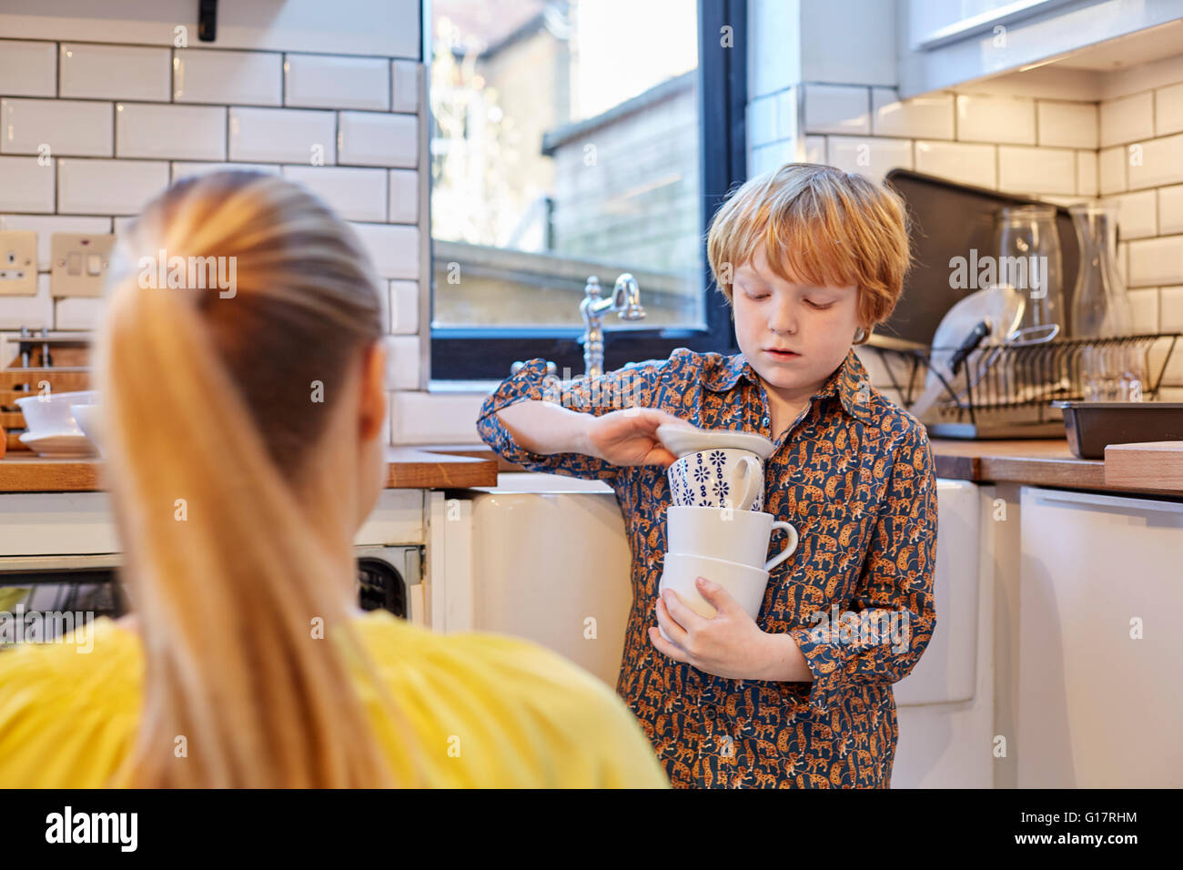 Boy carrying stack of mugs in kitchen Stock Photo