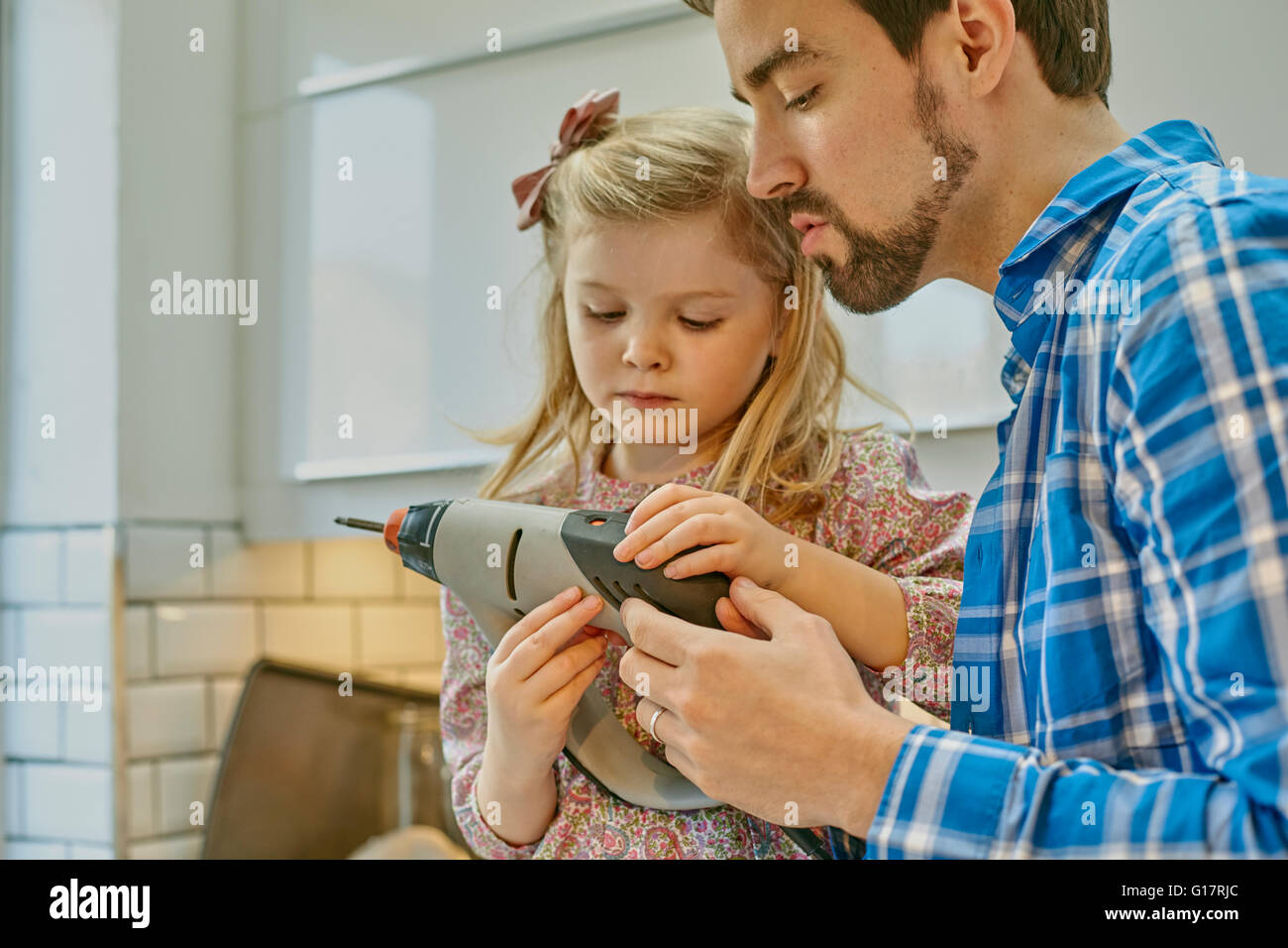 Father teaching daughter to use drill in kitchen Stock Photo