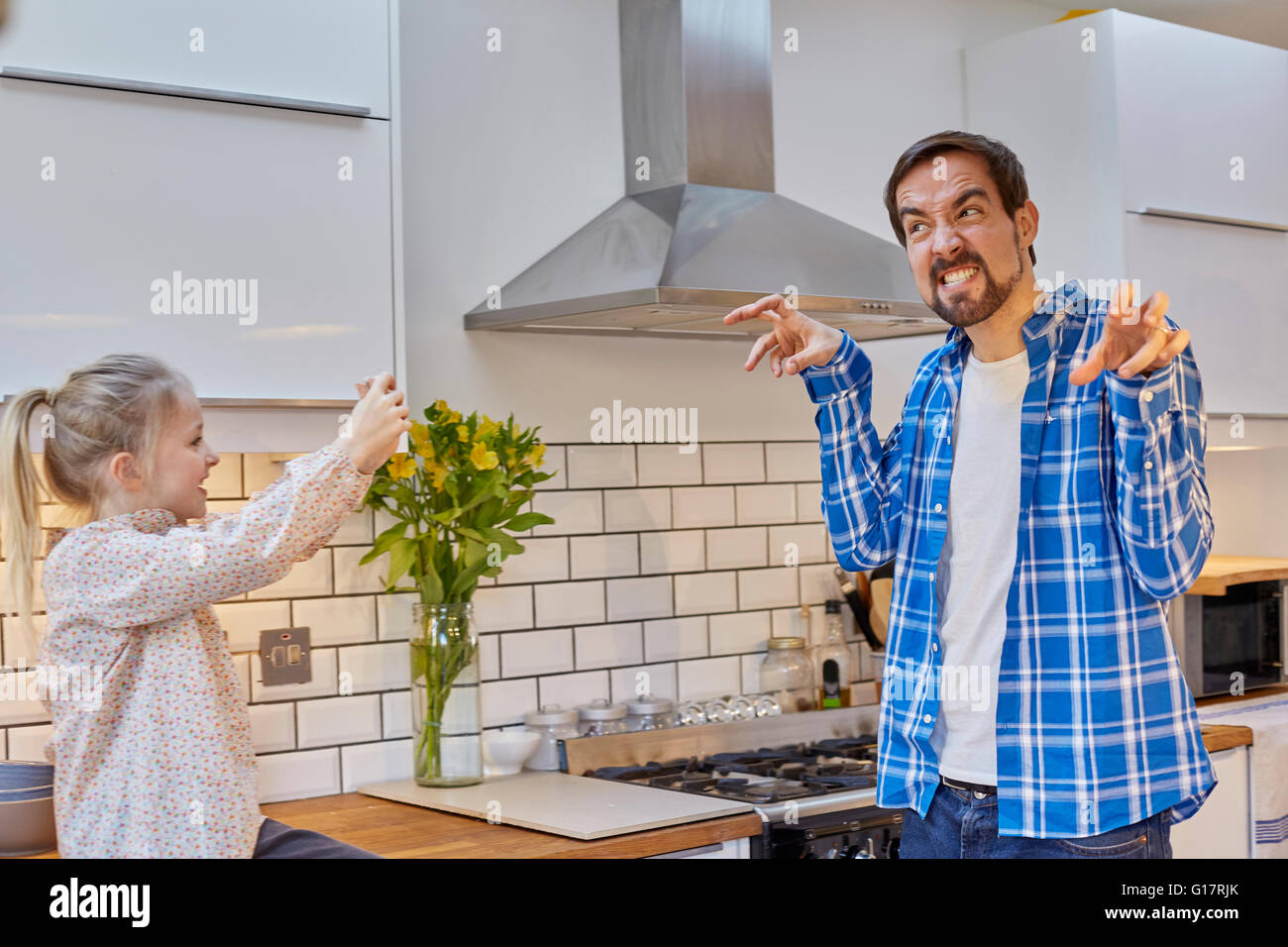 Daughter taking photograph of funny-faced father in kitchen Stock Photo
