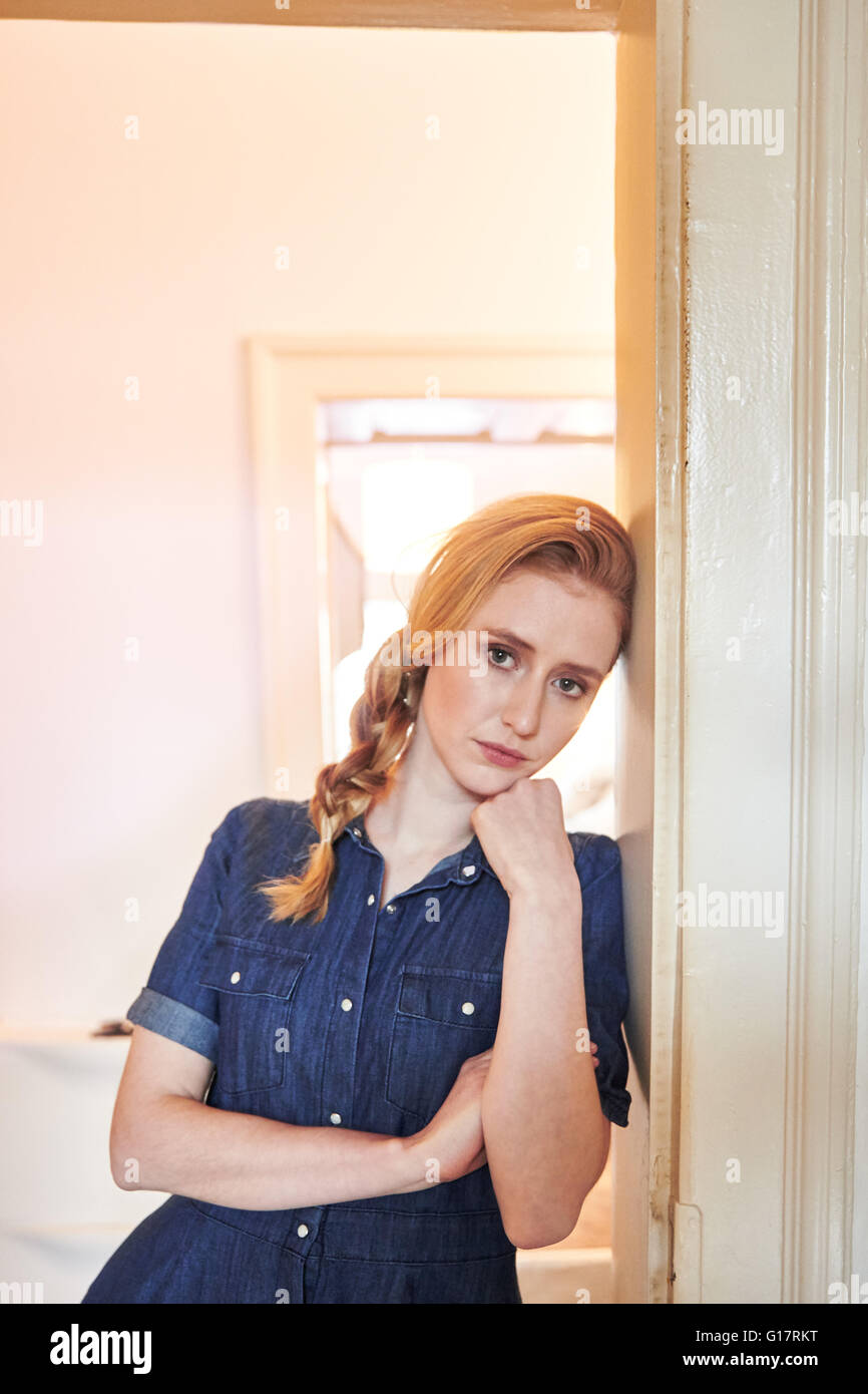 Portrait of sullen young woman leaning against doorway Stock Photo