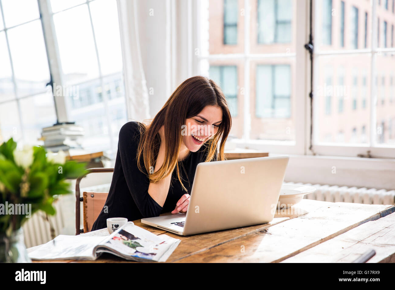 Young woman in city apartment laughing whilst working on laptop Stock Photo