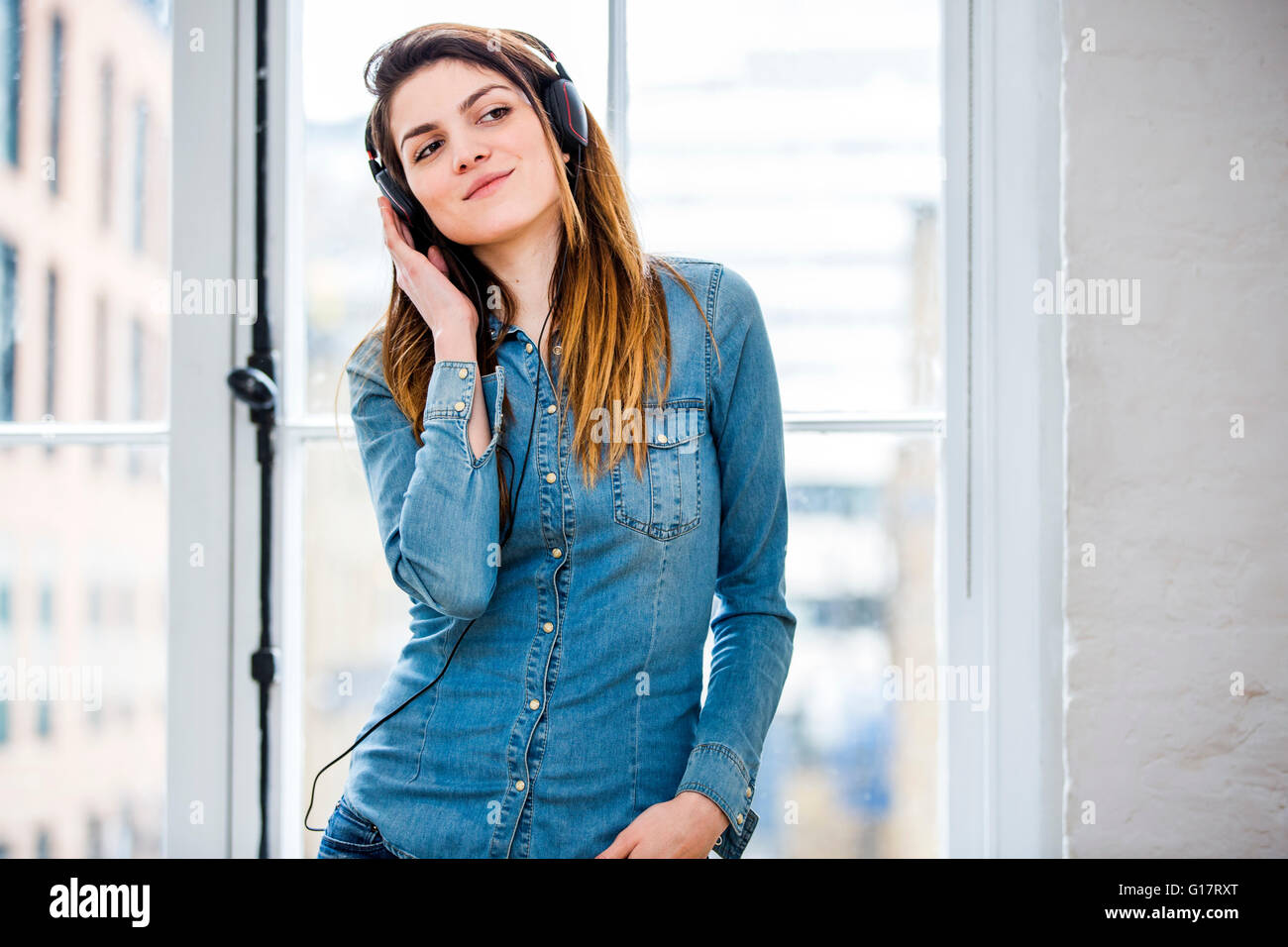 Beautiful young woman listening to music in front of city apartment window Stock Photo