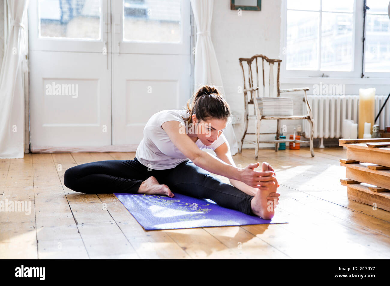 Young woman practicing yoga, touching toes in apartment Stock Photo