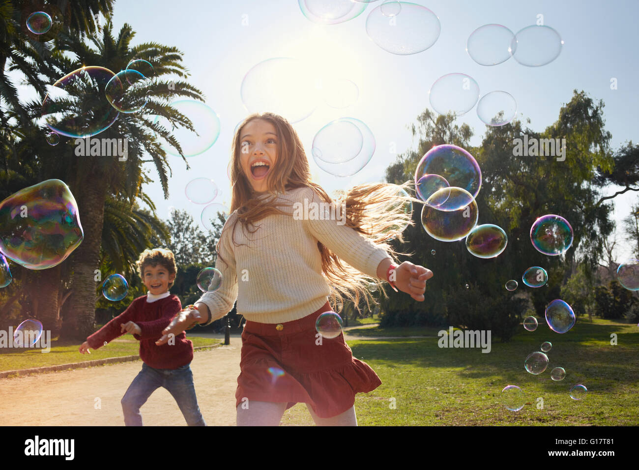 Girl and boy in park running after bubbles Stock Photo