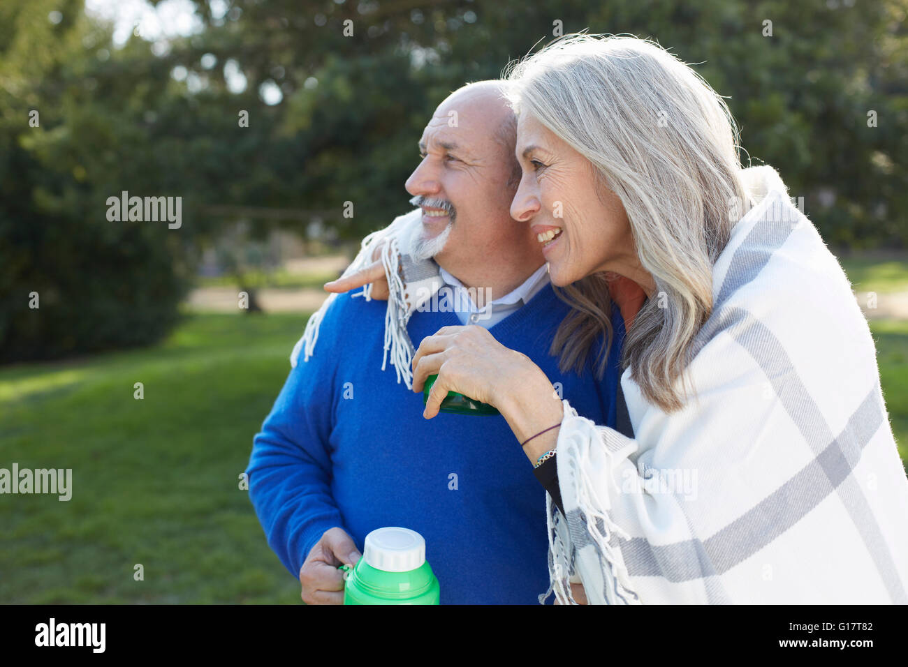 Couple wrapped in blanket holding drinks flask looking away smiling Stock Photo