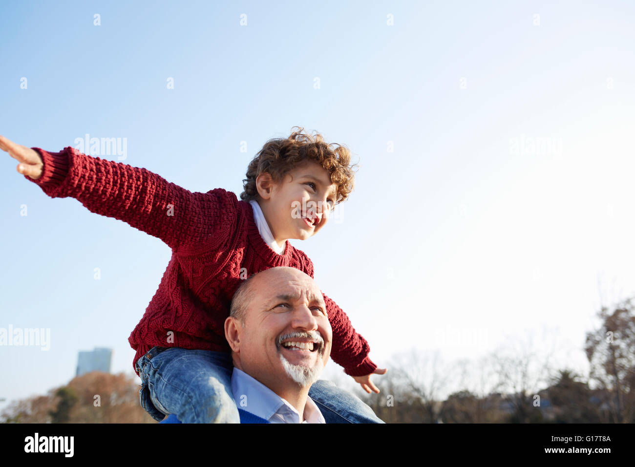 Grandson sitting on grandfathers shoulders, arms out smiling Stock Photo
