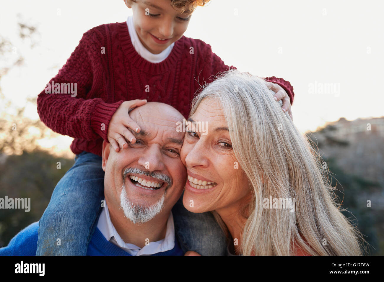Grandparents with grandson on shoulders looking at camera smiling Stock Photo