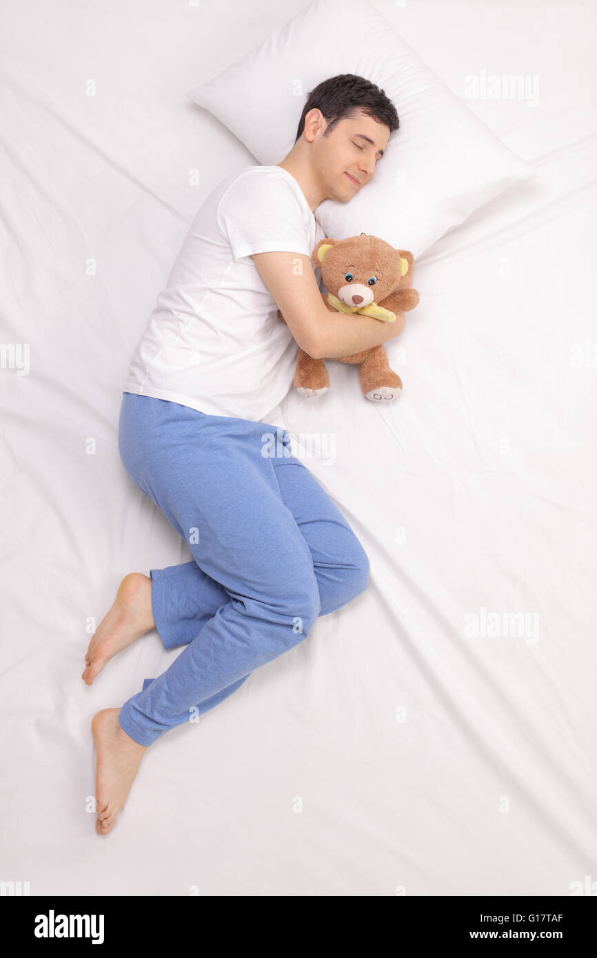 Vertical shot of a young childish guy sleeping on a bed with a teddy