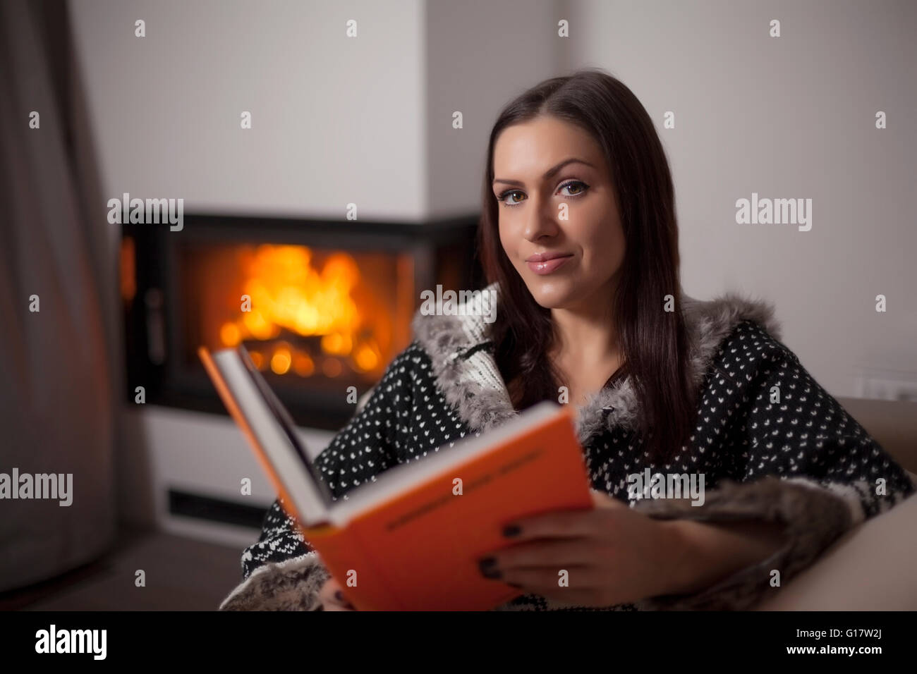 Portrait of beautiful woman reading book by fireplace Stock Photo