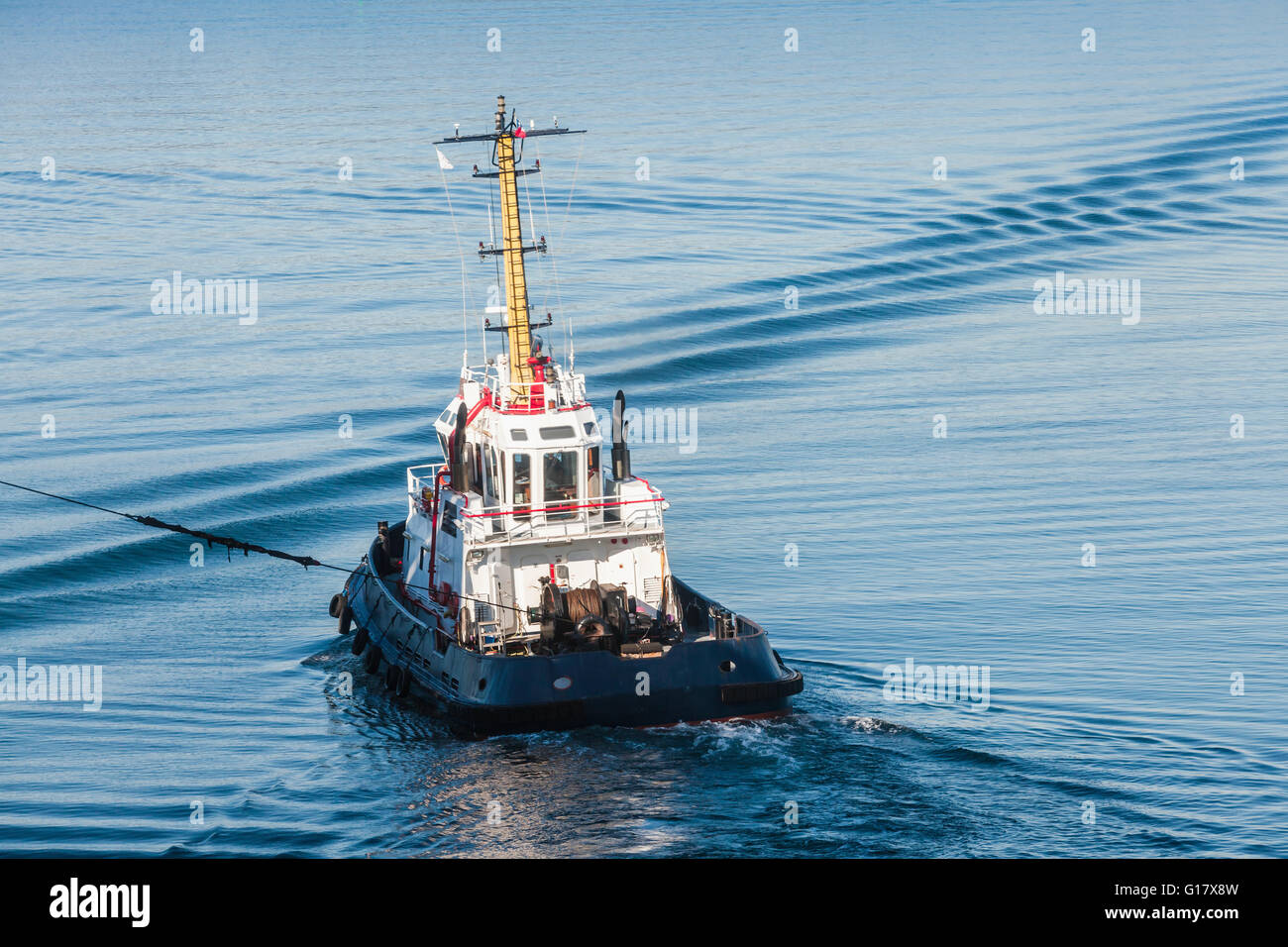 Tug boat with white superstructure underway pulling the rope, rear view Stock Photo