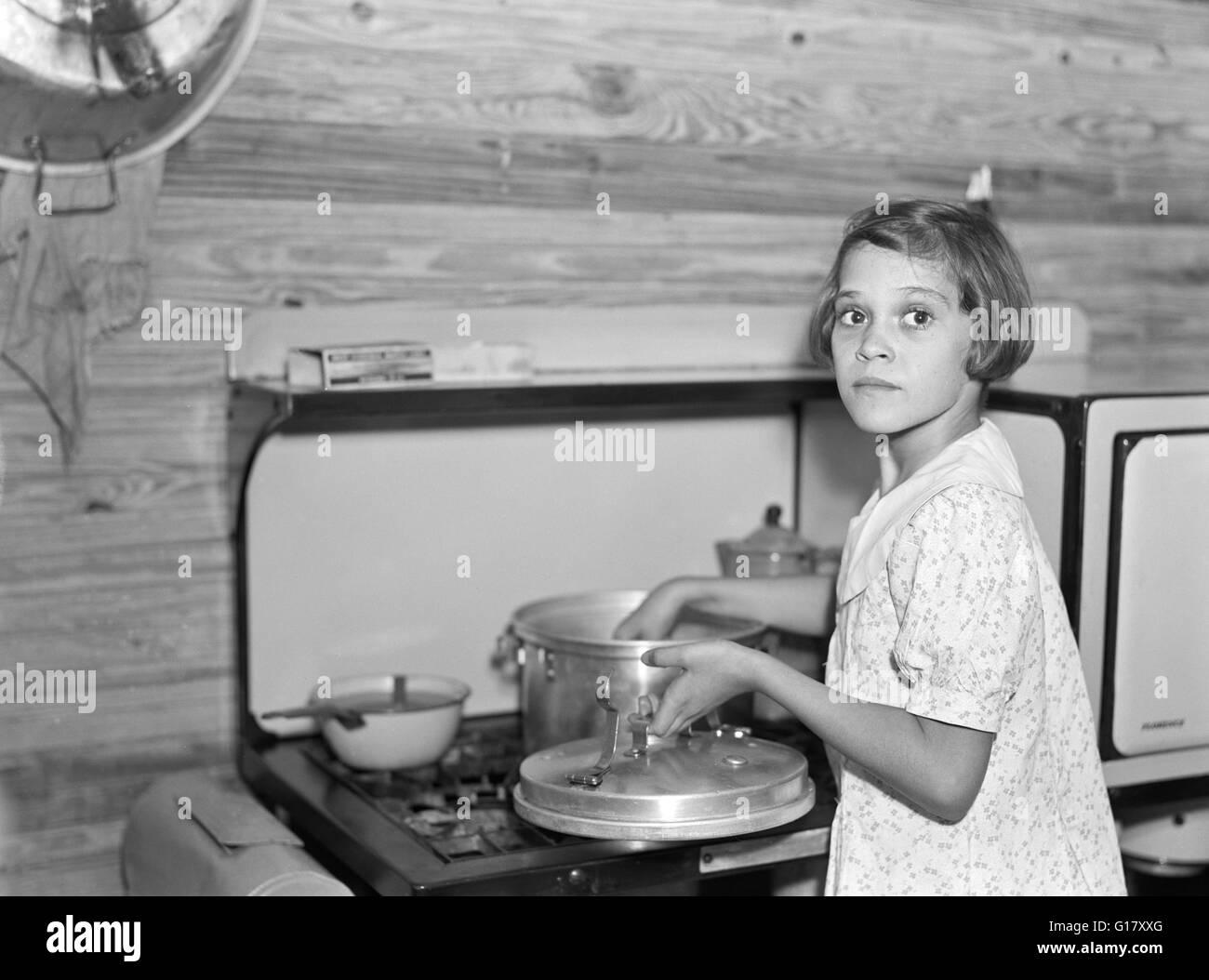 Young girl cooking while parents work at Citrus Packing Plant, Winter Haven, Florida, USA, Arthur Rothstein, U.S. Farm Security Administration, January 1937 Stock Photo