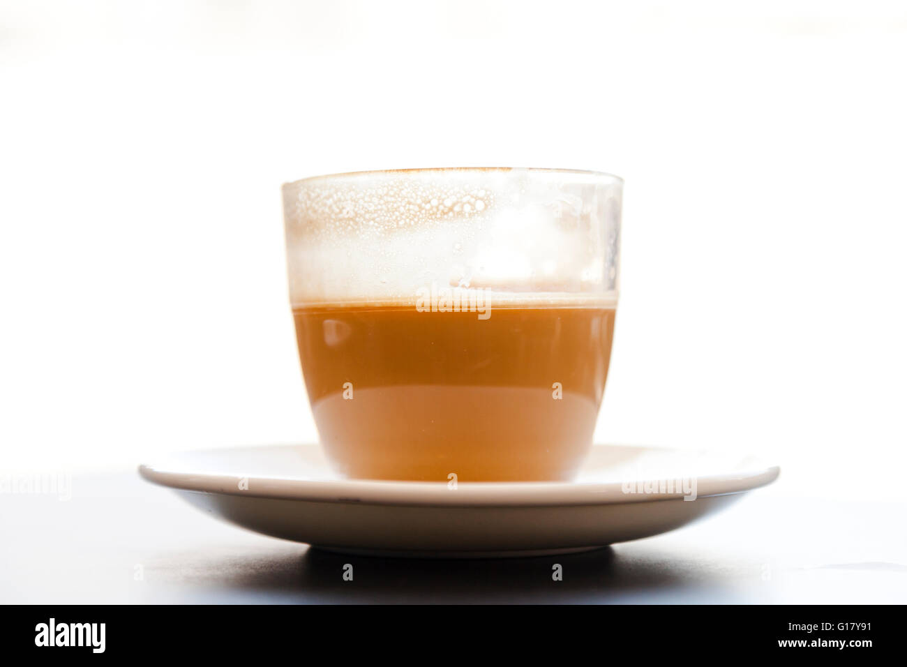 A glass half full of coffee,  cortado style viewed from the side against a whiet background Stock Photo