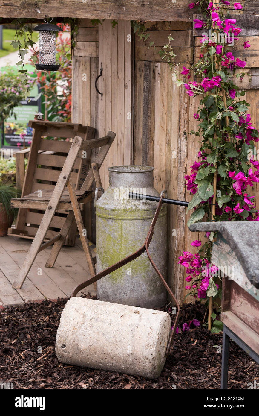 Harrogate Spring Flower Show 2016 (North Yorkshire, England) - rustic shelter, chairs, roller and milk churn, in the Wildlife Paradise' show garden. Stock Photo