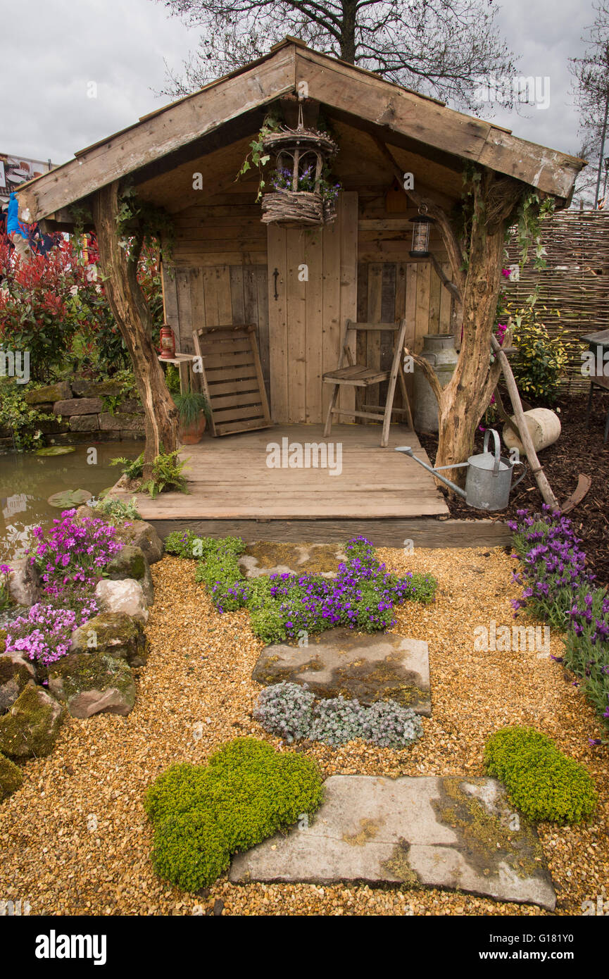 Harrogate Spring Flower Show 2016 (North Yorkshire, England) - rustic shelter, seating area, path and rockery in the Wildlife Paradise' show garden. Stock Photo