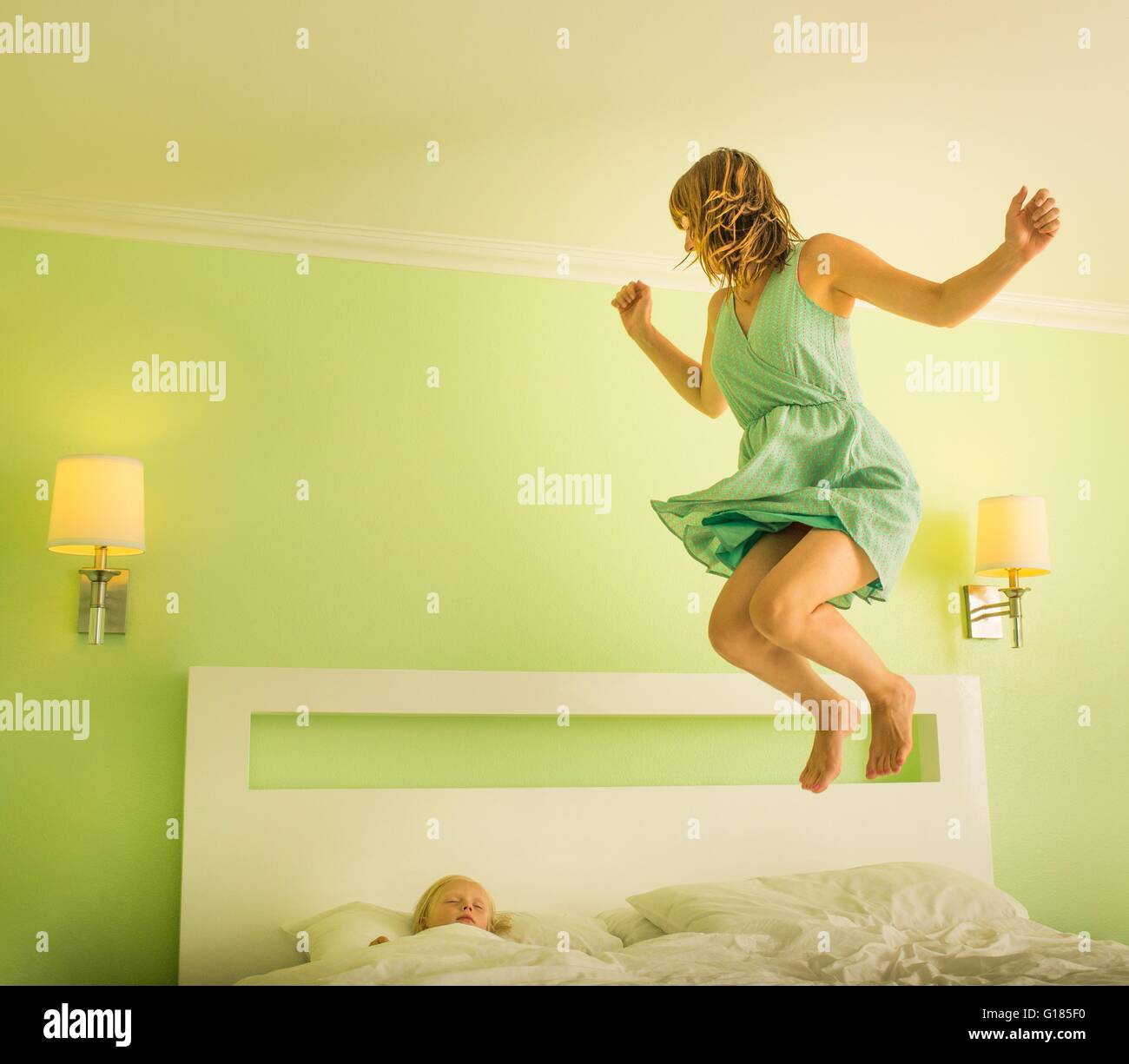 Mother jumping on bed to wake sleeping son Stock Photo