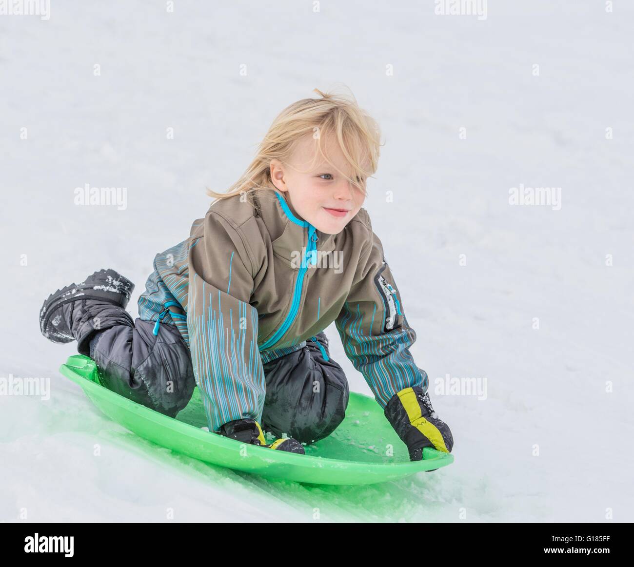 Boy playing on toboggan in snow Stock Photo