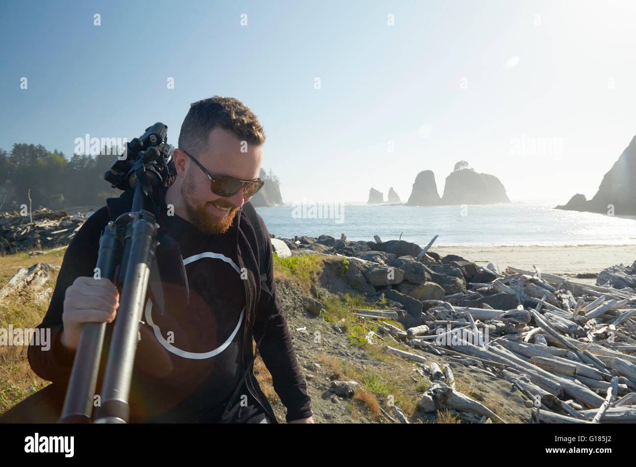 Male photographer carrying tripod on coast, Puget Sound, Washington