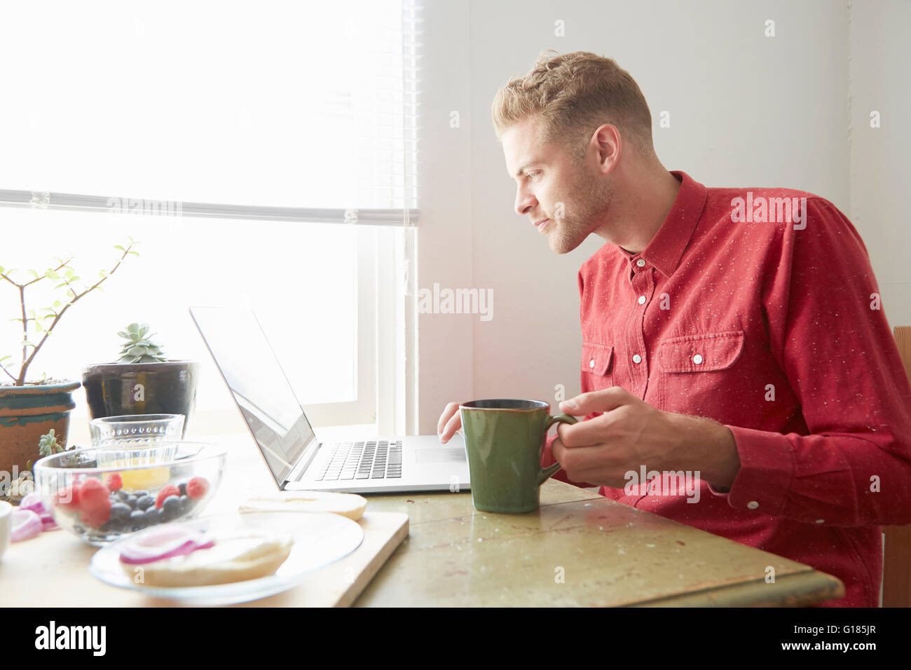 Young man sitting at dining table using laptop Stock Photo