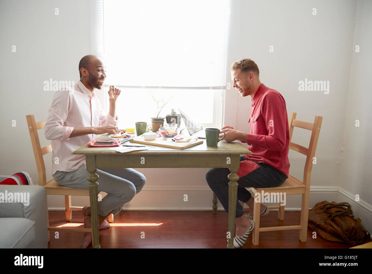 Side view of men sitting at dining table having breakfast laughing Stock Photo