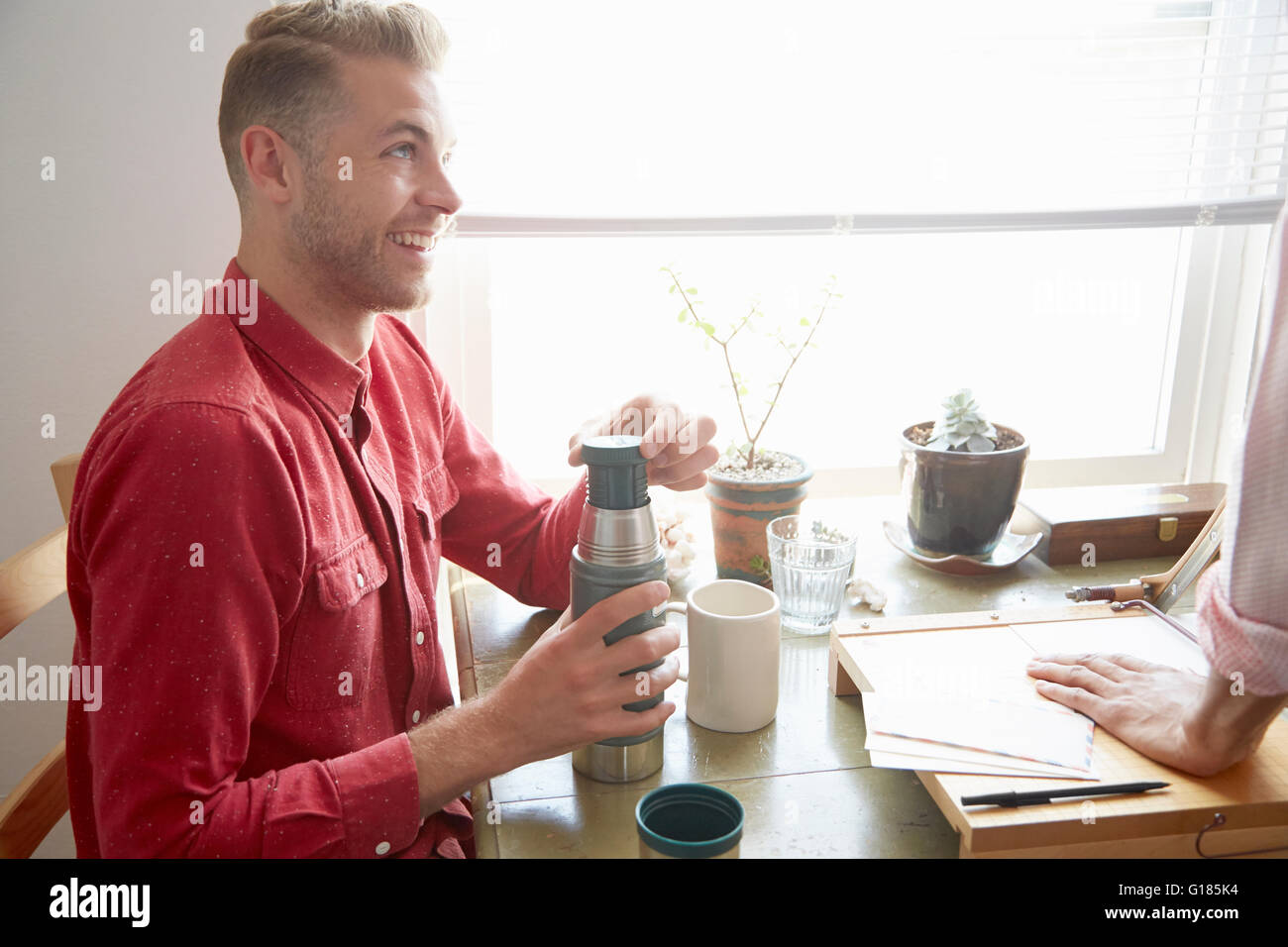Side view of man sitting at table holding flask smiling Stock Photo