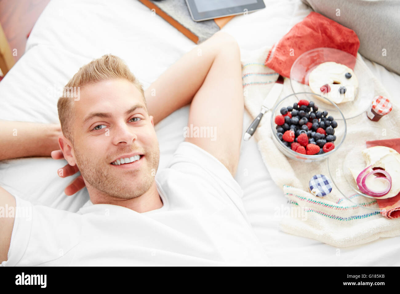 Man lying on bed, hands behind head looking at camera smiling Stock Photo