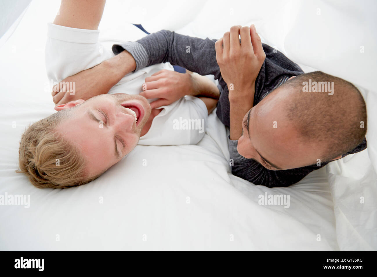 Homosexual couple fooling around on bed laughing Stock Photo